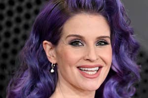 Woman with purple hair and black sheer outfit smiling
