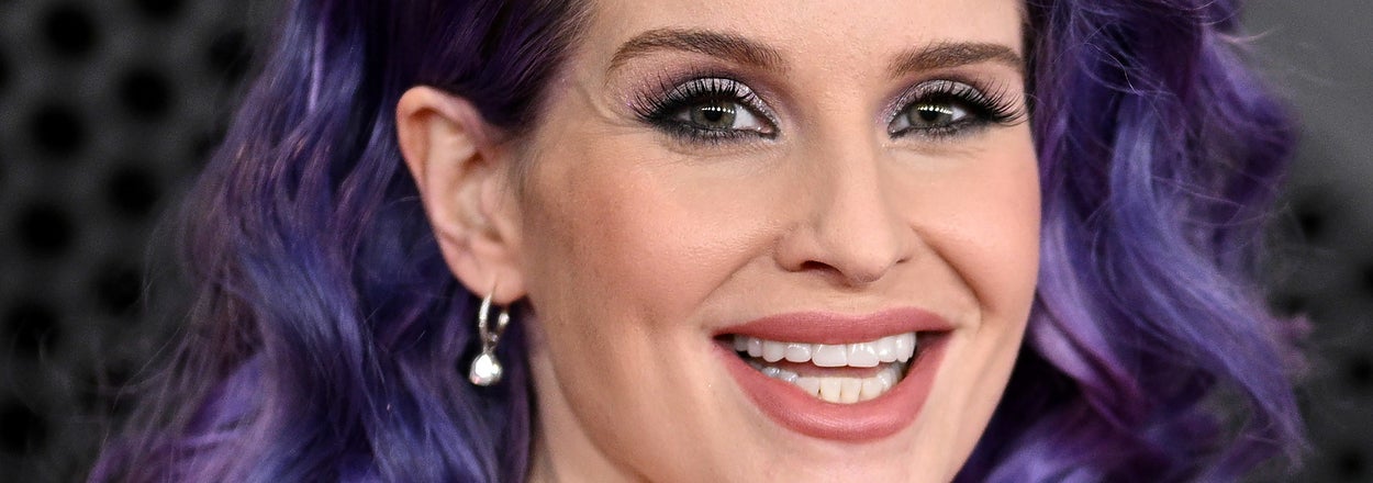 Woman with purple hair and black sheer outfit smiling
