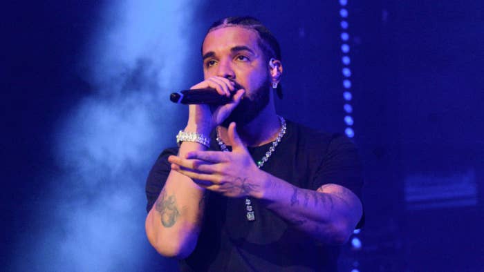 Drake performing on stage with a microphone, wearing casual attire and jewelry
