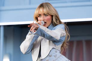 Person performing on stage with a microphone, wearing a stylized jacket and pants