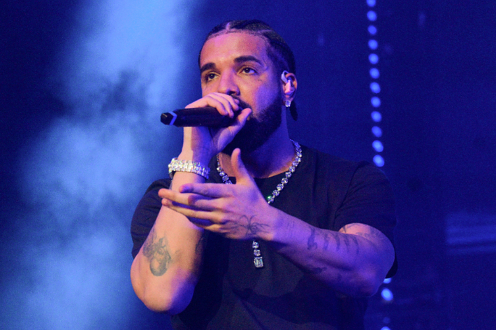 Drake performing on stage with a microphone, wearing casual attire and jewelry