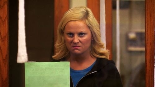 Character Leslie Knope from Parks and Recreation looks displeased while holding a document