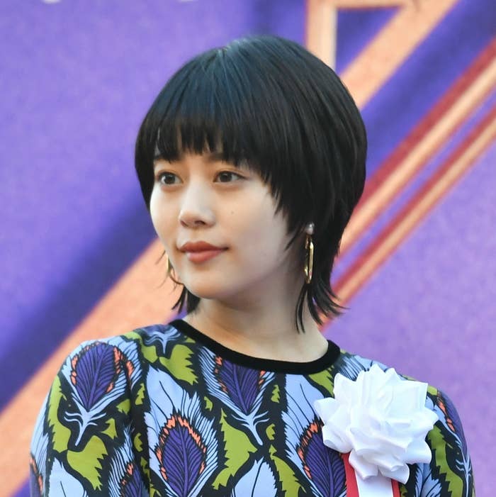 ボブカットの女性が、花柄のドレスと大きな白いリボンブローチを身につけています。