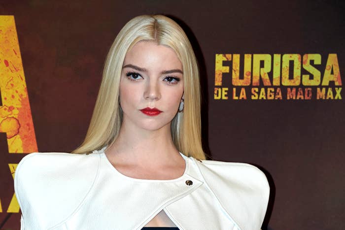 Anya Taylor Joy on red carpet in white outfit with structured shoulders, standing before a &#x27;Furiosa&#x27; backdrop