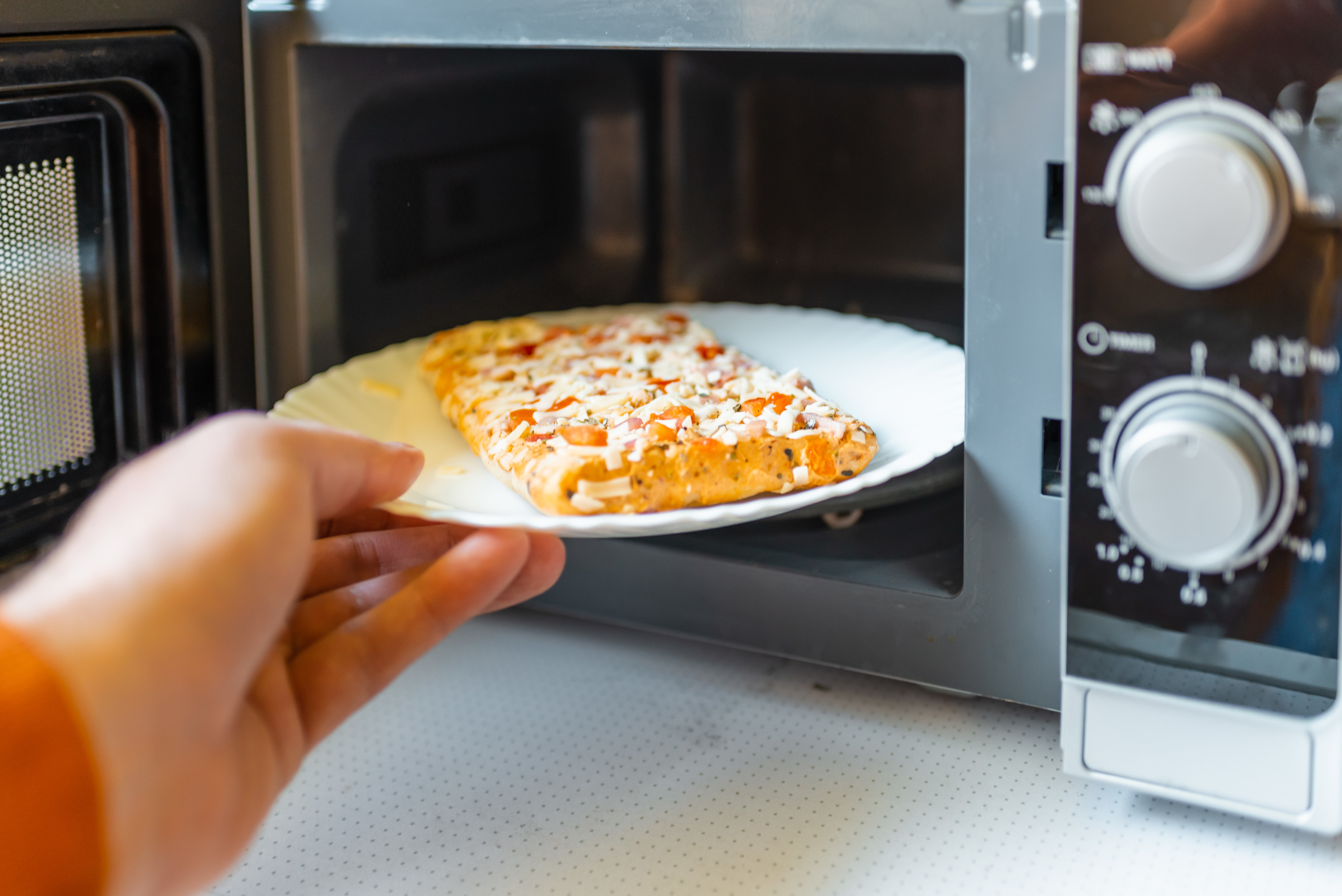 Person placing a slice of pizza on a plate into a microwave