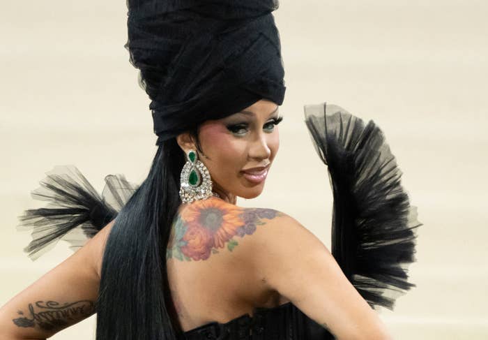 Cardi B in a gown with an oversized headpiece and feather details, posing on the Met Gala carpet