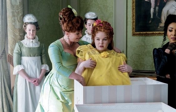Nicola Coughlan como Penelope Featherington en vestido amarillo siendo ayudada a vestirse por una doncella en una escena de época