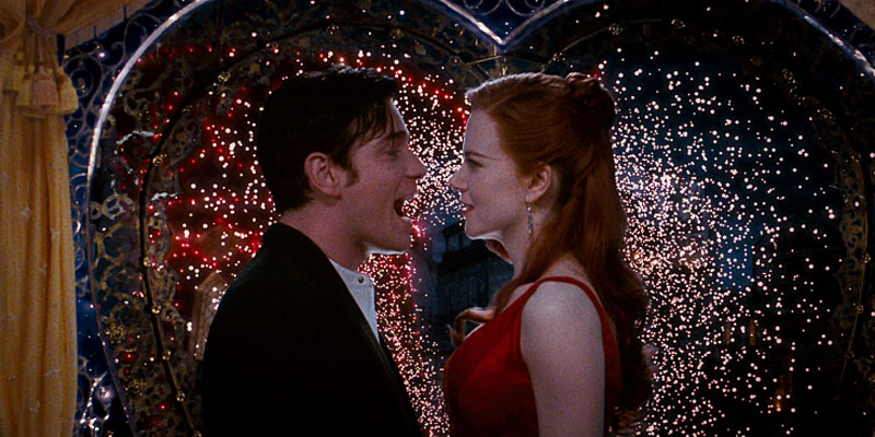 Two characters from the film Moulin Rouge, a man in a suit and a woman in a red dress, share a gaze