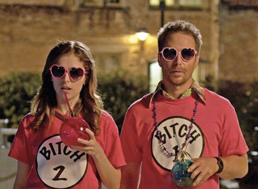 Two people wearing matching heart-shaped sunglasses and T-shirts labeled &quot;BITCH 1&quot; and &quot;BITCH 2&quot; holding drinks