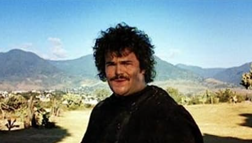 Jack Black with a mustache wearing a black shirt, outdoors with hills in the background