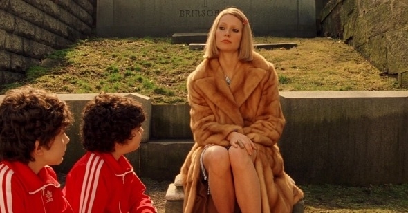 Woman in fur coat sits on steps with two boys in red jackets beside her