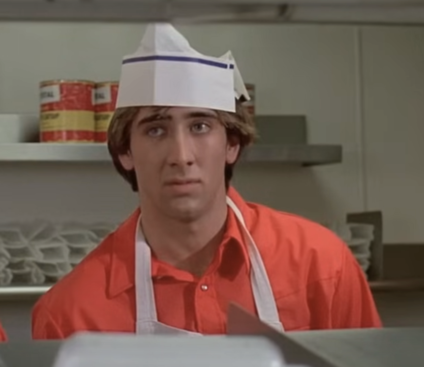 in a scene, Nic in a chef&#x27;s hat and apron appears concerned in a kitchen setting