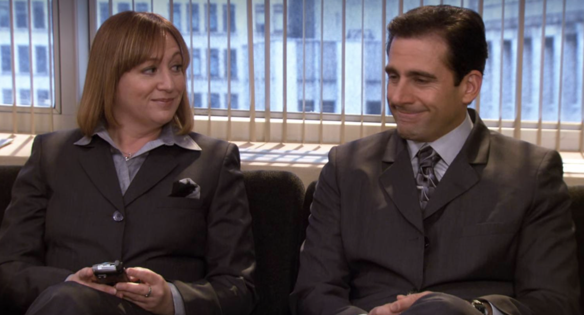 Two characters from &quot;The Office&quot; sitting side by side, smiling slightly, dressed in business attire