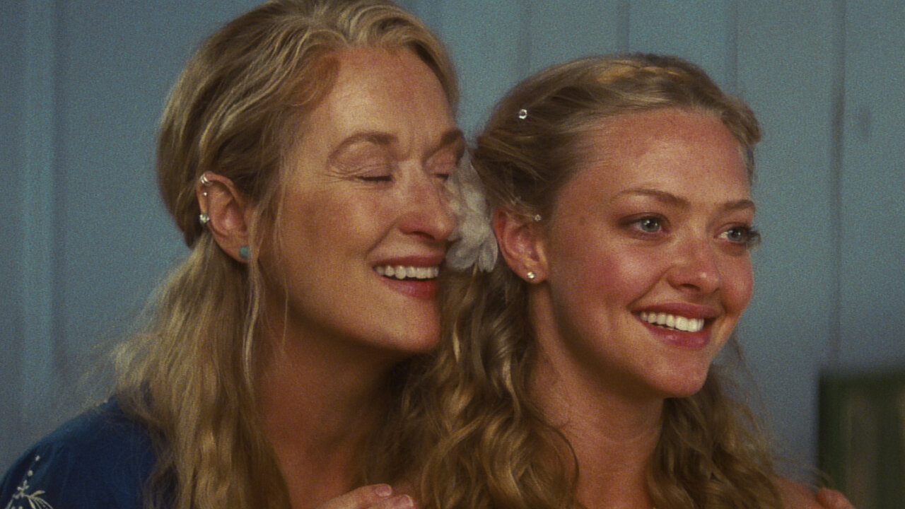 Two women smiling close together, one younger with a flower in her hair