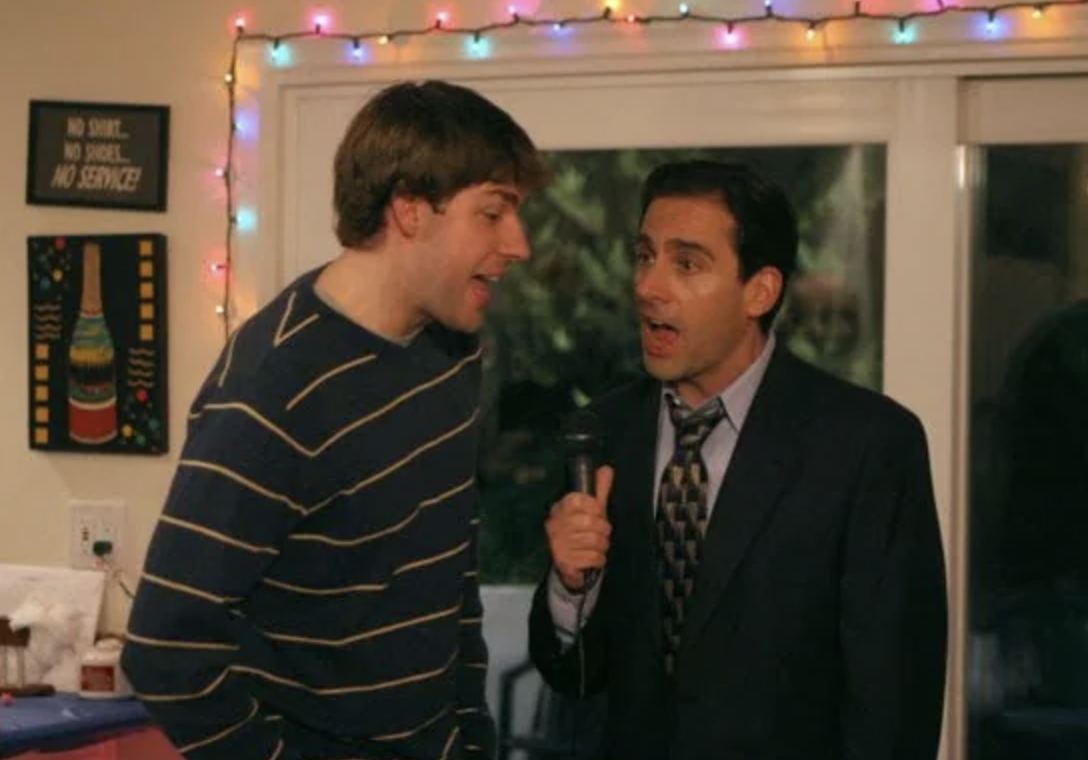 Two characters from &quot;The Office&quot; during a party scene, one holding a microphone