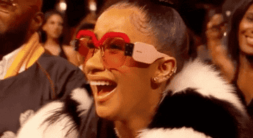 Cardi B in unique glasses and a fur coat laughing joyfully at an event