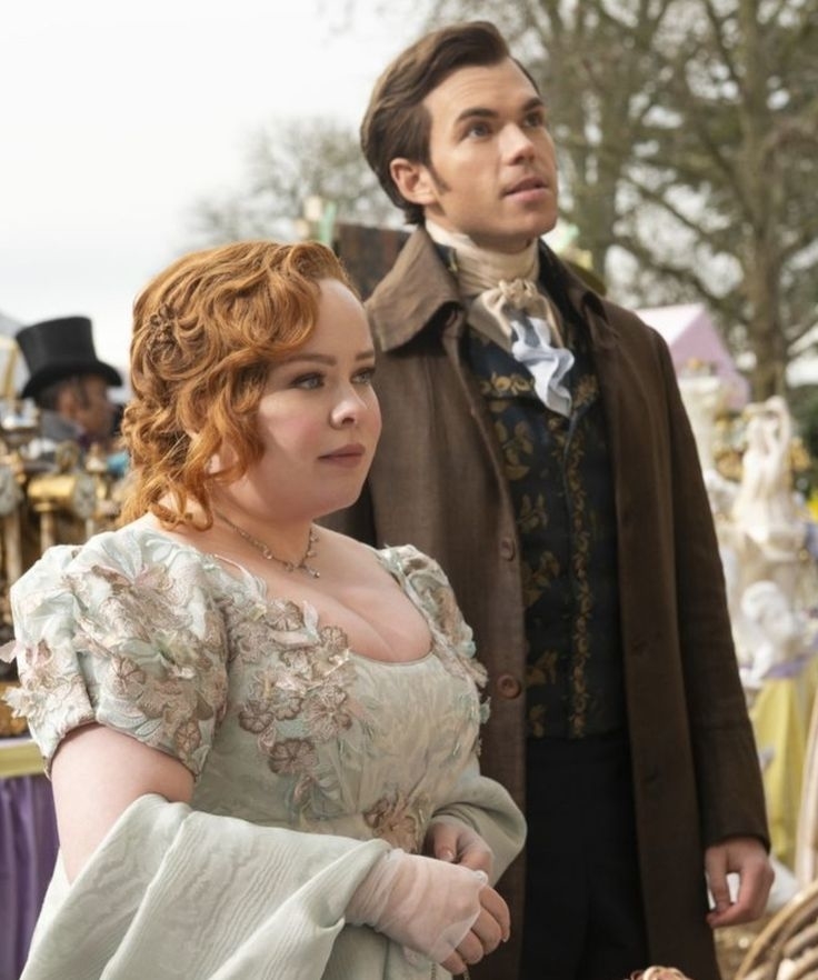 Personajes de Bridgerton, la mujer en vestido de época floral y el hombre en abrigo oscuro con chaleco estampado