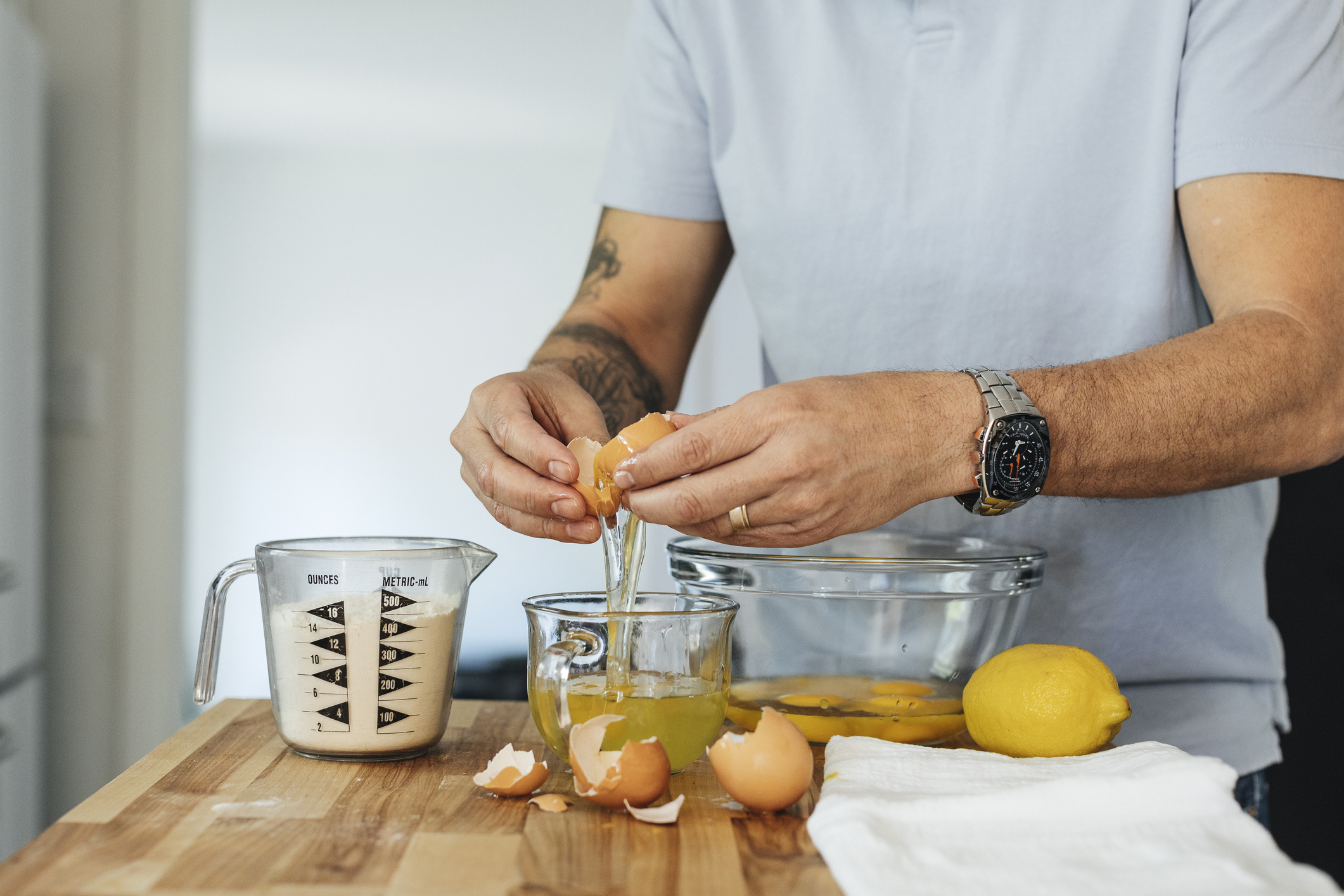 Person cracking an egg into a glass bowl on a kitchen counter with lemons and a measuring cup nearby