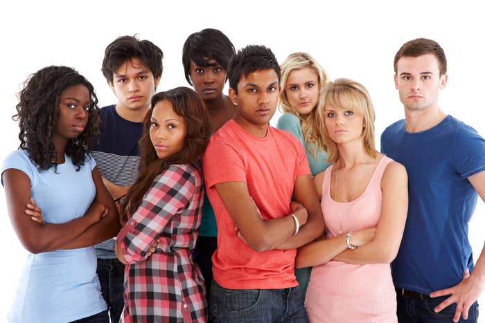 Group of seven diverse young adults standing with arms crossed, expressing seriousness