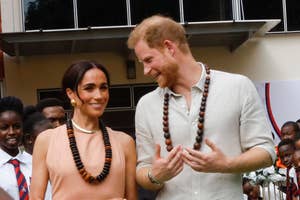 Prince Harry and Meghan Markle watch traditional dancers perform, both smiling and clapping, engaged in the cultural event