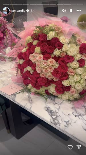 A massive, round floral arrangement with a variety of roses on a table, with a person partially visible in the background