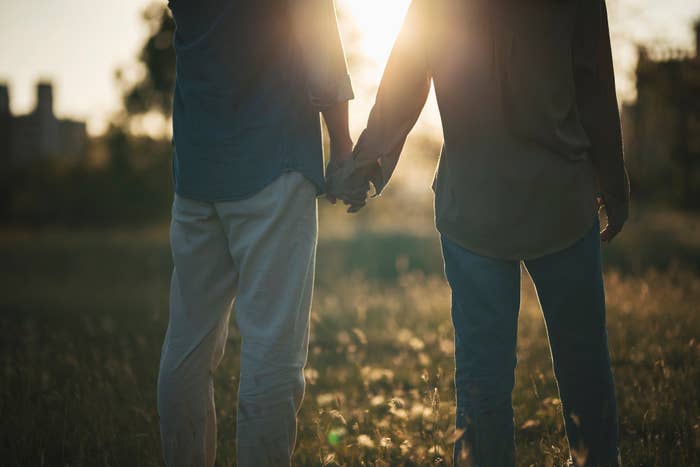Two people holding hands, standing in a field, backlit by the setting sun