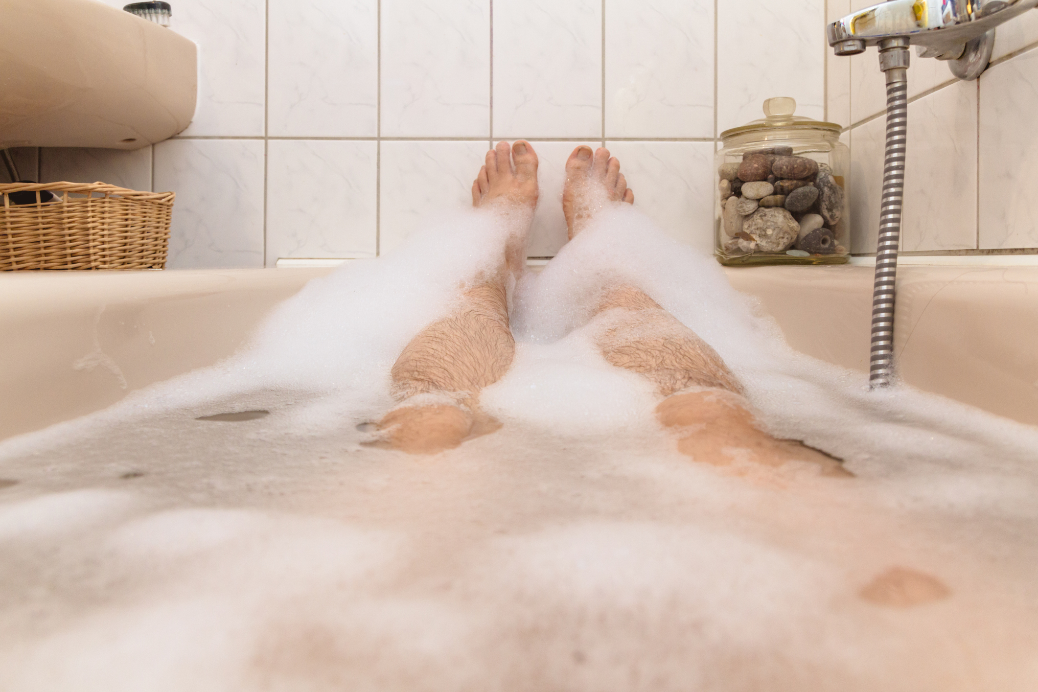 Two legs are visible resting in a bubble bath with surrounding bathroom decor