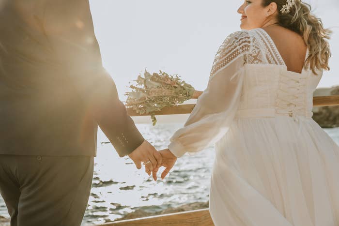 Bride and groom holding hands by the sea, bride's dress has lace details