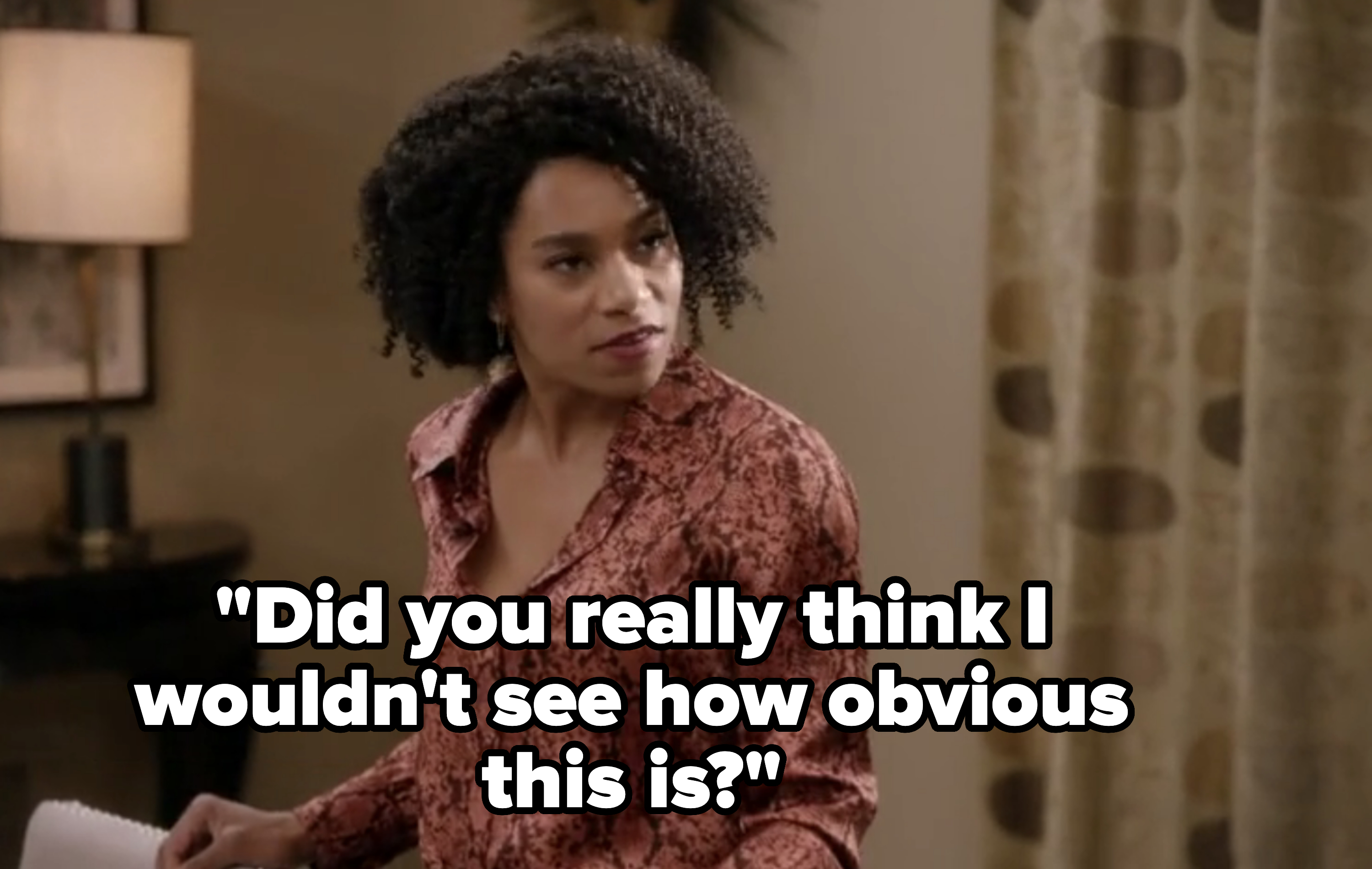 Woman with curly hair in a patterned blouse indoors, looking pensive with paper in hand