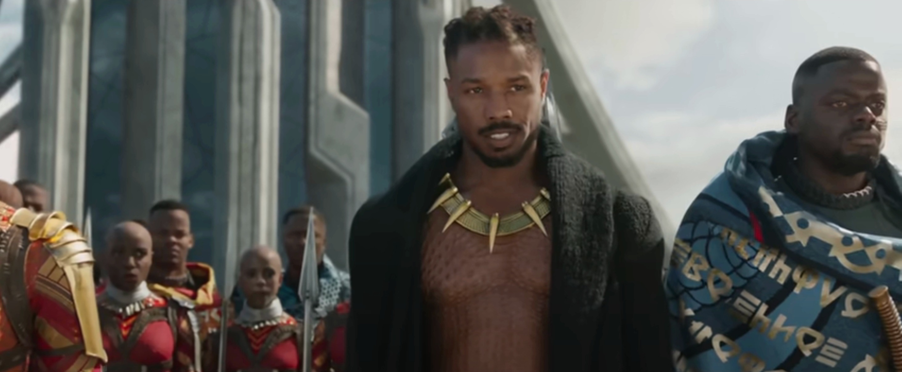 Michael as Kilmonger, wearing an open coat and Wakandan necklace, surrounded by guards