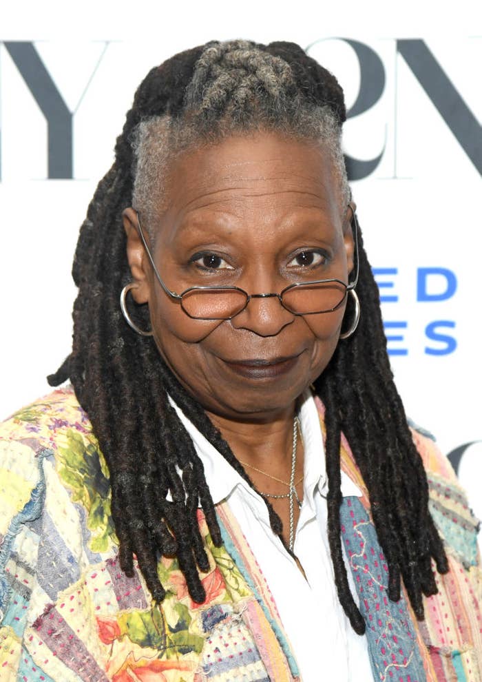 Whoopi Goldberg poses at an event, wearing glasses and a patterned jacket