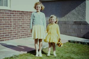 Two smiling girls posing outside, one holding a stuffed toy, in casual dresses