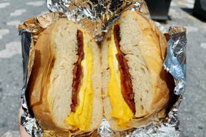 Hands holding a foil wrapped bagel sandwich with bacon, egg, and cheese