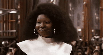 Whoopi Goldberg smiling in a white and black outfit at an event