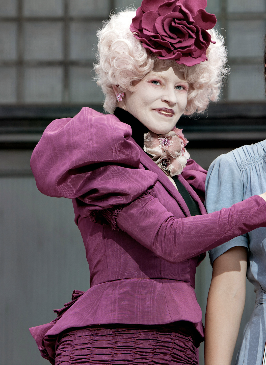 Effie Trinket from The Hunger Games, wearing a ruffled dress with matching hat