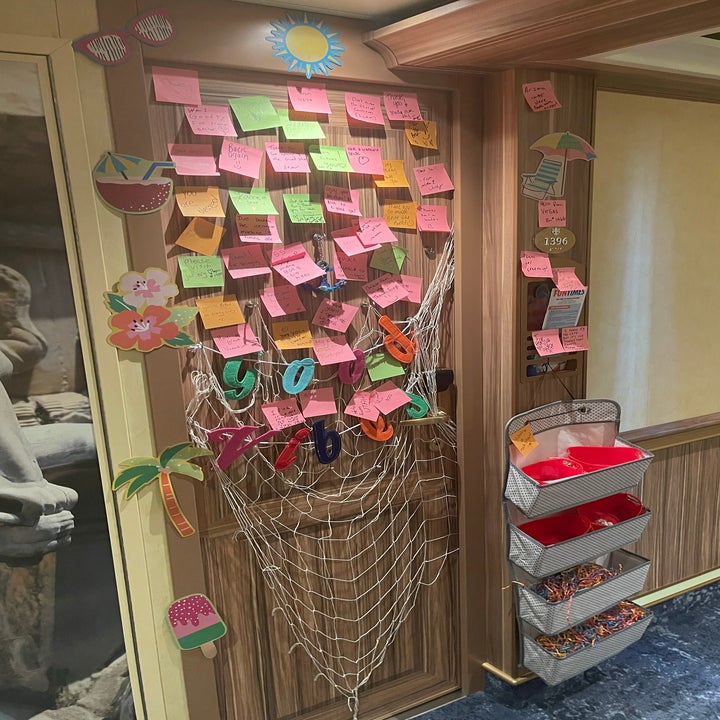 Bulletin board with numerous sticky notes, a net with words "joy", and assorted hanging decorations