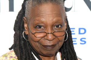 Whoopi Goldberg poses at an event, wearing glasses and a patterned jacket