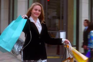 Character Cher from 'Clueless' smiles while holding shopping bags on a street