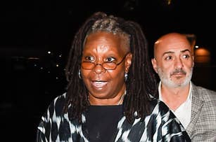 Whoopi Goldberg in a patterned coat, walking with a man in a checked jacket