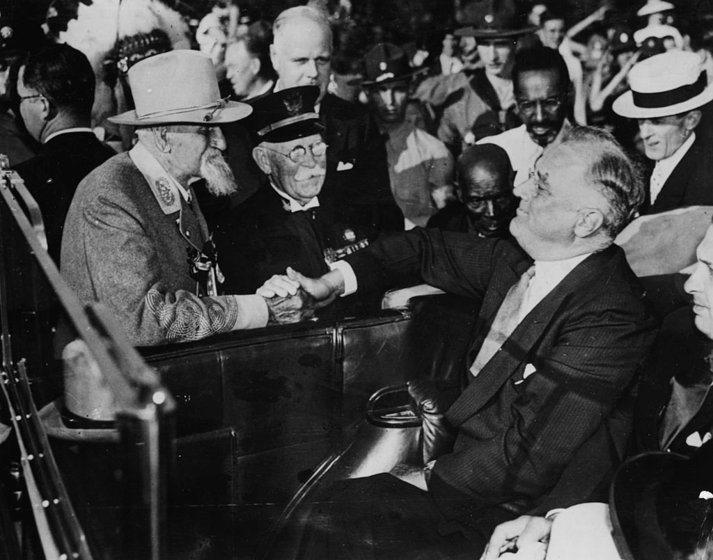 Two elderly men shaking hands in a car at a historic event