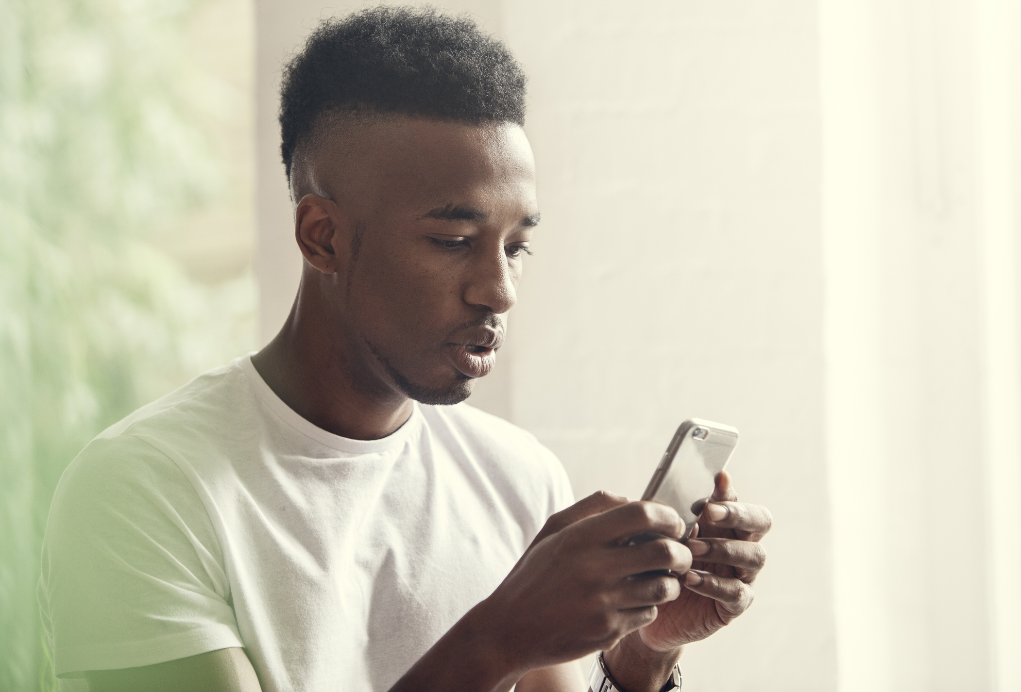 Man in a white shirt using and looking intently at a smartphone
