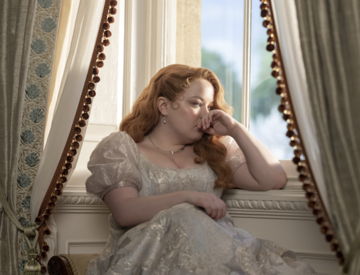 Personaje de la serie Bridgerton reflexionando junto a una ventana, vestido con traje de época