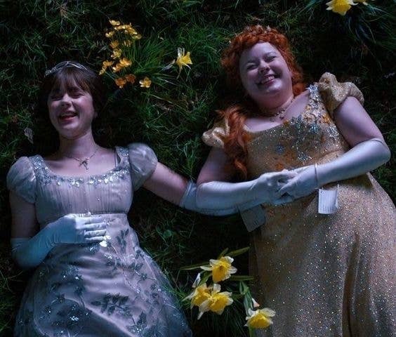 Dos personajes de película, vestidas de princesas, acostadas en el pasto con flores