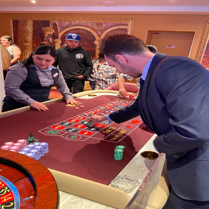 Man in a suit placing chips on a roulette table at a casino, dealer and others present