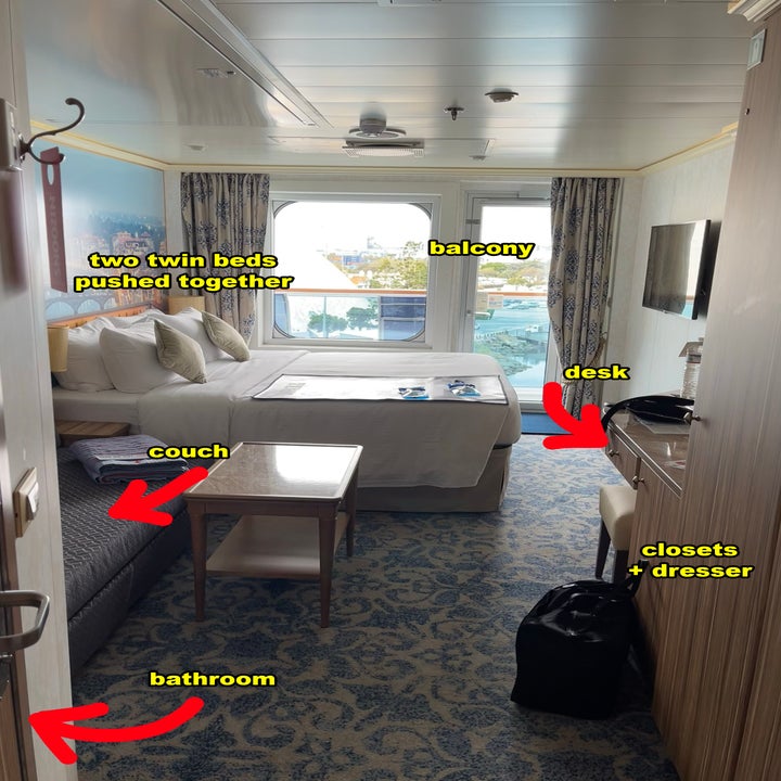 Cruise ship cabin with two twin beds together, balcony, desk, couch, bathroom, closets, and a dresser