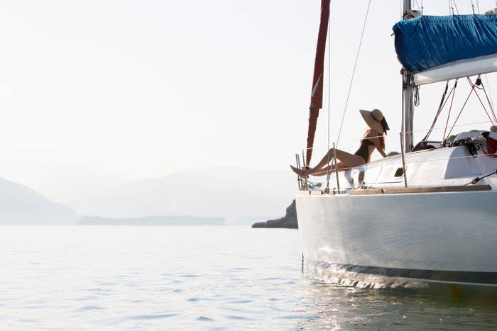 Person relaxing on a sailboat with mountains in the background, symbolizing financial freedom