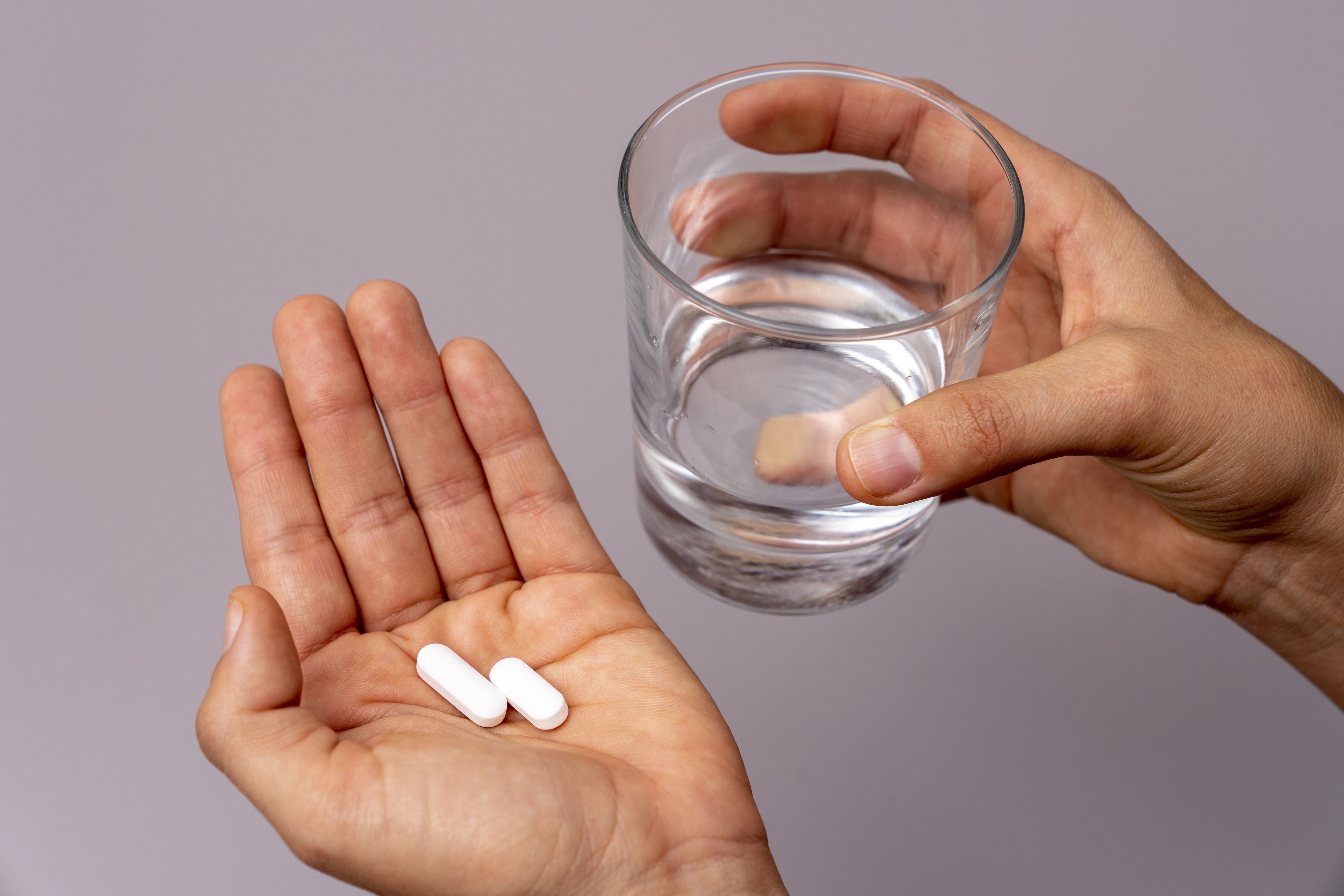 Hand holding pills with another hand holding a glass of water, implying medication or health management in a workplace