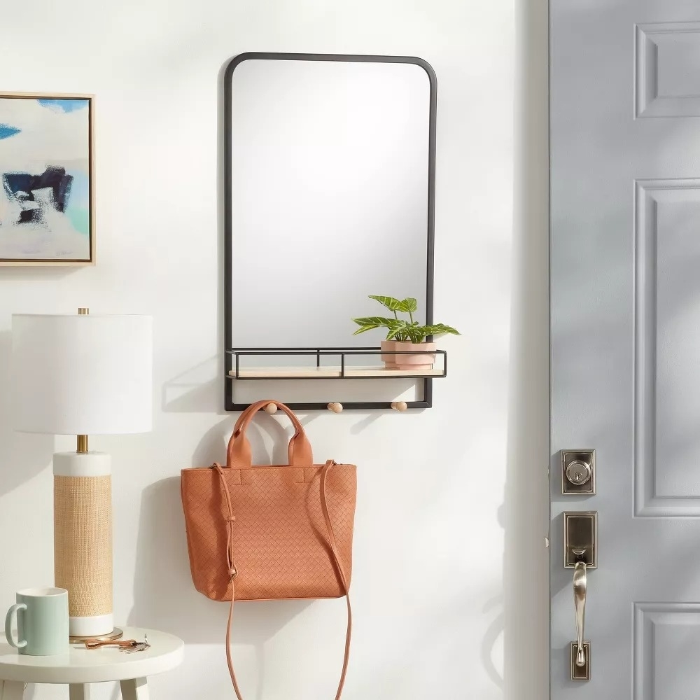 Wall-mounted mirror with a shelf holding a plant and a woven tote bag