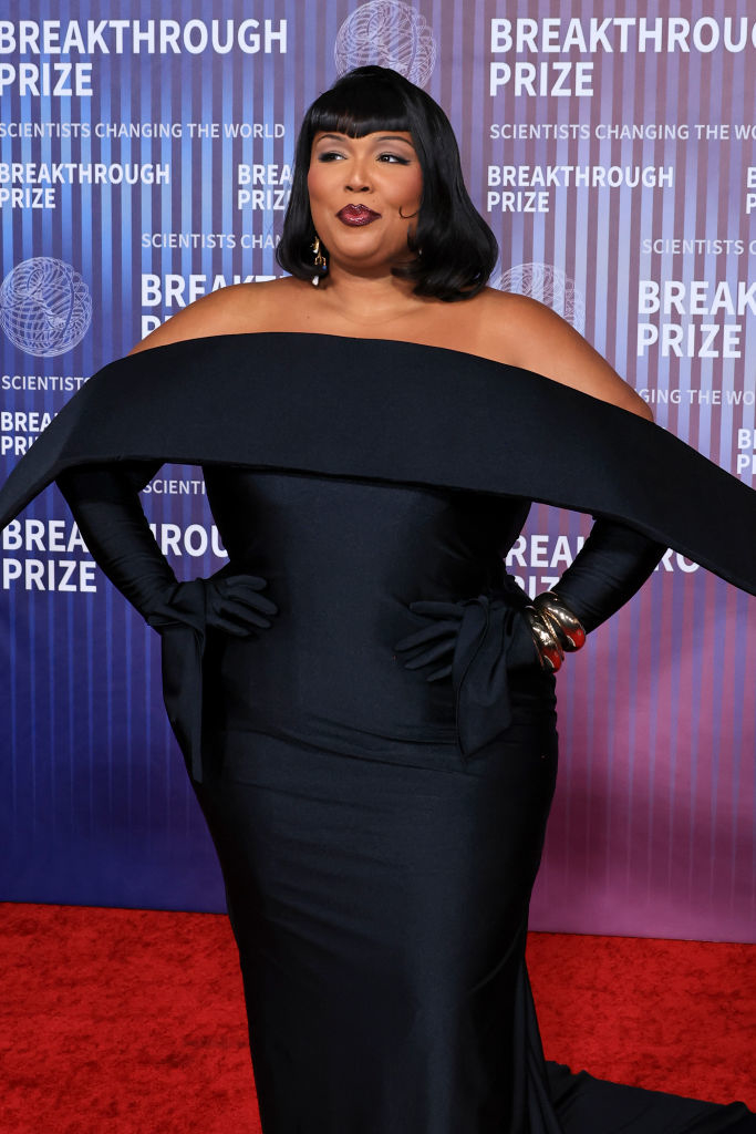 Lizzo posing on the red carpet in an off-the-shoulder gown with dramatic sleeves and gloves