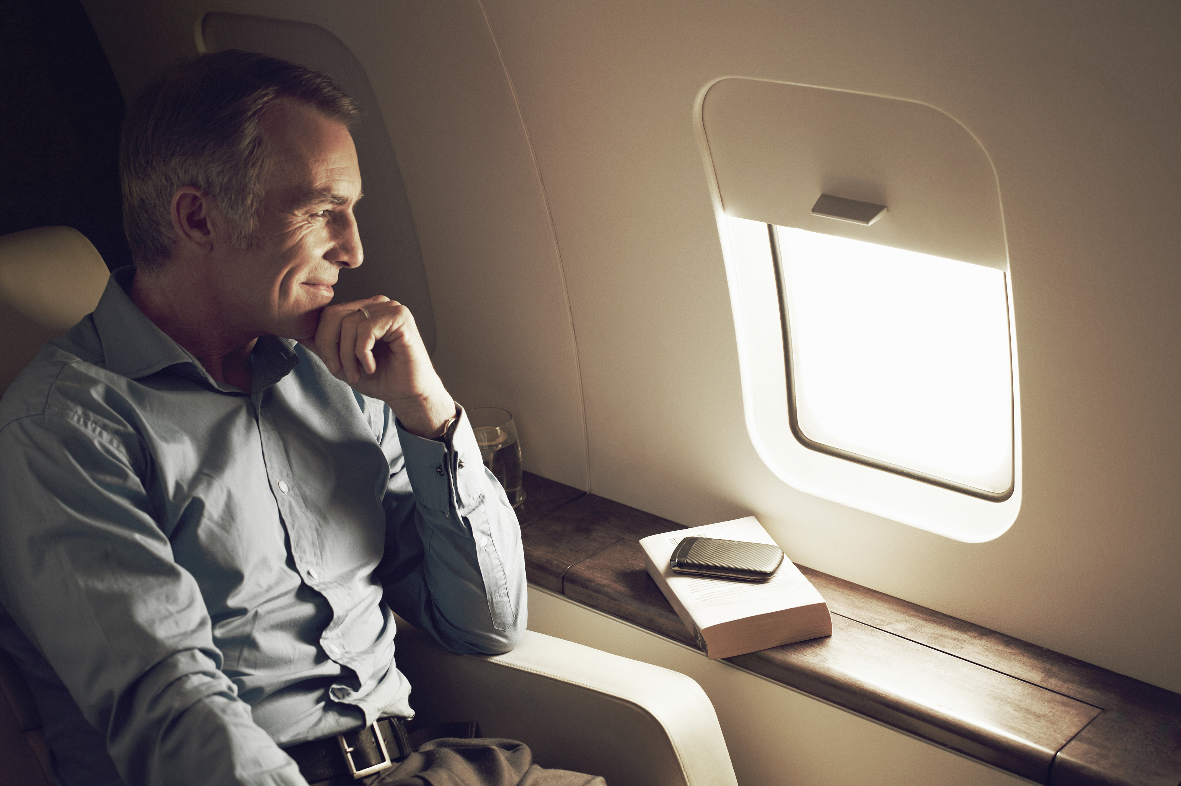 Man in business attire sitting thoughtfully by airplane window with a closed laptop on the table next to him
